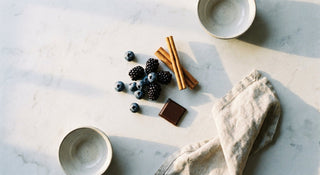 Overhead flat lay of dark berries, cinnamon sticks, and dark chocolate on a pale stone surface, evoking mindful control over sugar cravings.
