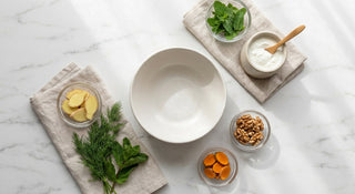 A flat-lay of fresh ginger, fennel, green herbs, and yogurt arranged on a white marble surface in soft natural light, evoking digestive wellness and gut health.